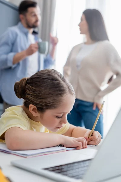 Расплывчатая пара разговаривает рядом дочь пишет в блокноте во время выполнения домашней работы — стоковое фото