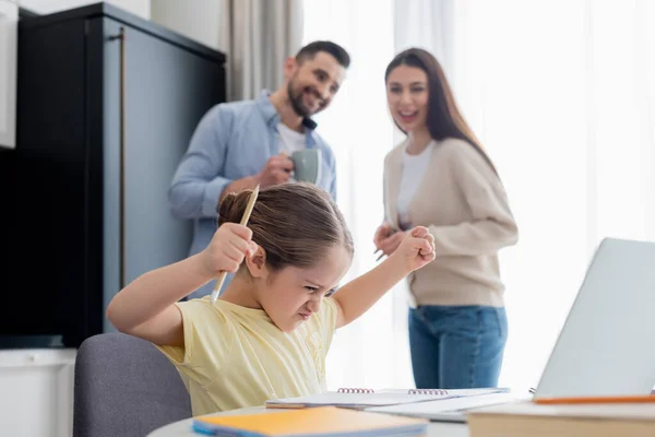 Verschwommenes Paar lächelt neben wütendem Mädchen und zeigt geballte Fäuste bei Hausaufgaben — Stockfoto