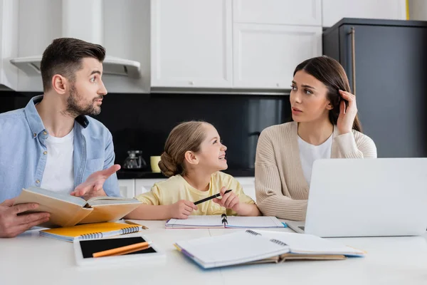 Discouraged husband and wife looking at each other while doing homework with daughter — Stock Photo