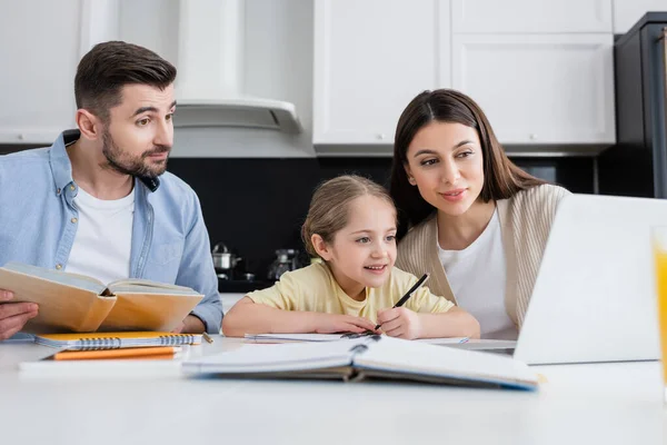Mädchen mit Eltern schaut auf Laptop, während sie gemeinsam Hausaufgaben machen — Stockfoto