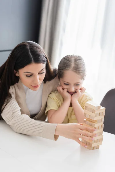 Mother showing how to play wood blocks game to daughter at home — Stock Photo