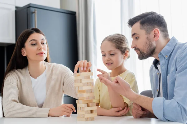 Father and daughter pointing with fingers while mother removing block from wooden tower — Stock Photo