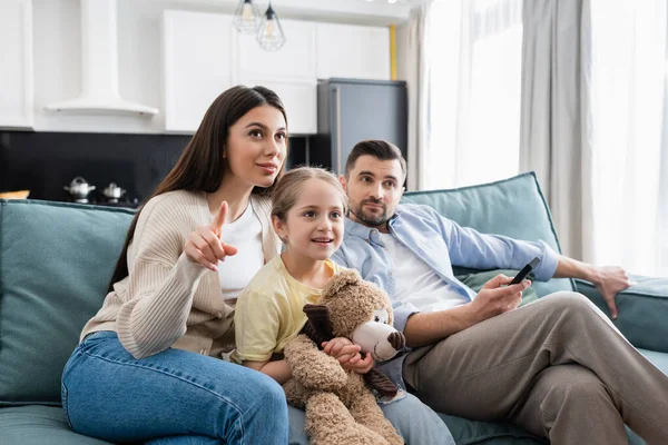 Woman pointing with finger while watching tv with husband and daughter — Stock Photo