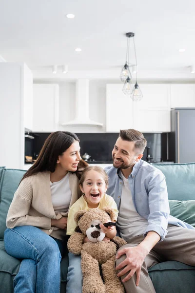 Genitori felici che si guardano mentre guardano film comici vicino a figlia eccitata — Foto stock