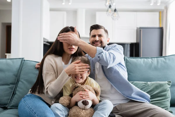 Familia asustada cubriendo los ojos el uno al otro mientras ve película de terror cerca de oso de peluche - foto de stock