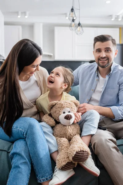 Lachendes Mädchen mit Teddybär beim Komödienfilm mit glücklichen Eltern — Stockfoto