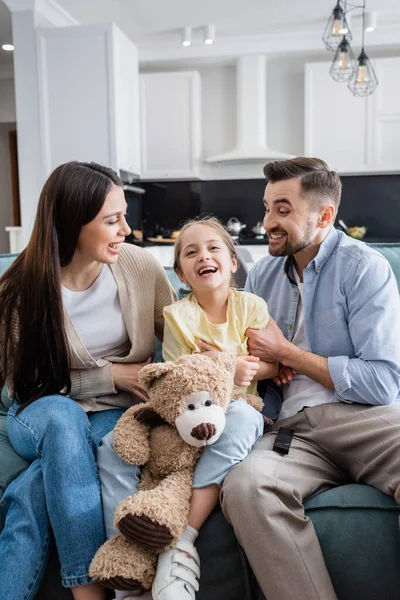 Excité fille rire tout en regardant film comédie près de parents gais et ours en peluche — Stock Photo