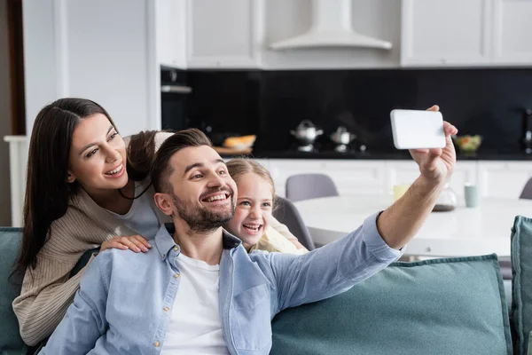 Alegre hombre tomando selfie en celular con feliz esposa e hija - foto de stock