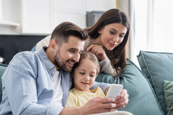 Happy man using mobile phone near daughter and wife at home — Stock Photo