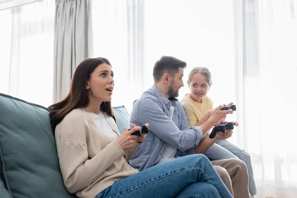 KYIV, UKRAINE - APRIL 8, 2021: worried woman playing video game with husband and daughter — Stock Photo