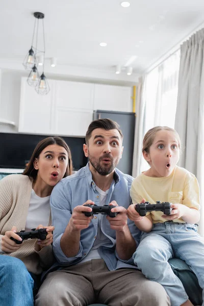 KYIV, UCRANIA - 8 de abril de 2021: familia asombrada jugando videojuegos juntos en casa - foto de stock