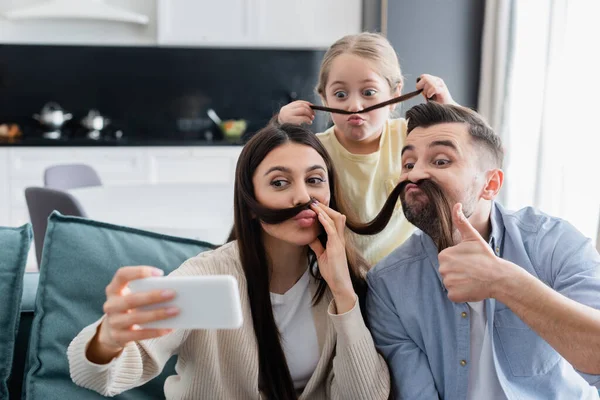 Woman taking selfie with family having fun while imitating mustache with her hair — Stock Photo