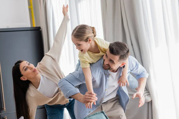 Woman imitating plane while excited daughter piggybacking on back of dad — Stock Photo