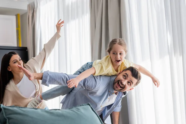 Excited child piggybacking on fathers back and imitating plane with mother — Stock Photo