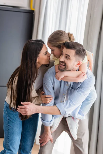 Girl pouting lips with mom while piggybacking on back of cheerful father — Stock Photo