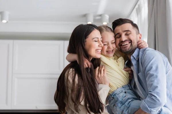 Glückliche Eltern und Tochter mit geschlossenen Augen, die sich zu Hause umarmen — Stockfoto