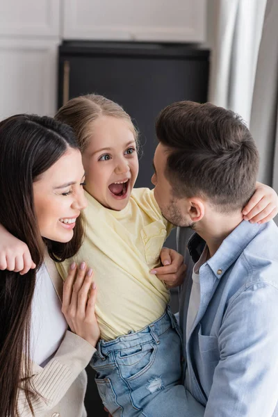 Excited girl with open mouth in hands of happy parents — Stock Photo