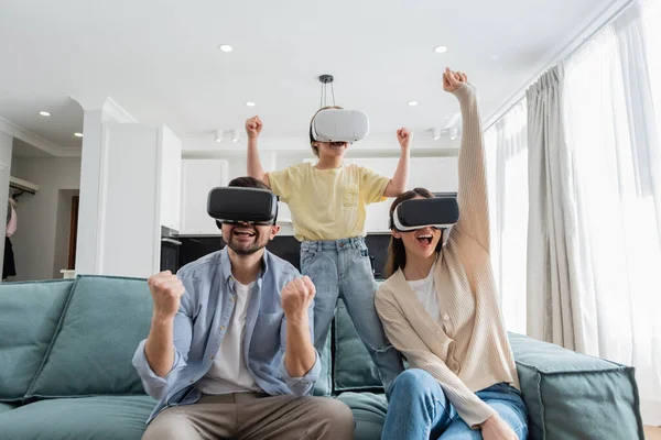 Fröhliche Familie zeigt Siegergeste beim Spielen in vr-Headsets im Wohnzimmer — Stockfoto