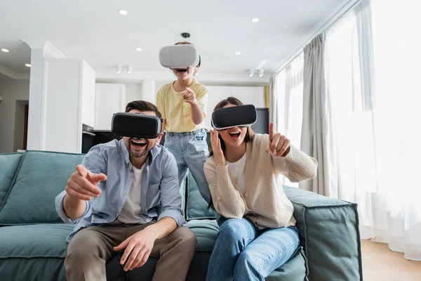 Amazed parents with daughter pointing with fingers while gaming in vr headsets — Stock Photo