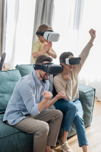 Pareja emocionada mostrando gesto de éxito mientras juega en auriculares vr con su hija - foto de stock