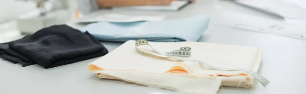 Measuring tape and samples of tissue on desk in tailor shop, banner — Stock Photo