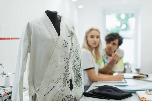 Blurred designers looking at kimono with traditional drawing on mannequin in tailor shop — Stock Photo