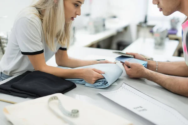 Cropped view of designers looking at tissue and color palette near sewing pattern, blurred foreground — Stock Photo