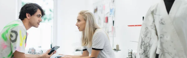 Vue latérale de jeunes designers parlant près de mannequin flou dans l'atelier de mode, bannière — Photo de stock