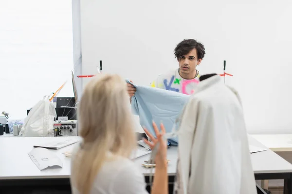 Back view of blurred designer gesturing while talking to colleague with fabric sample — Stock Photo