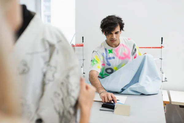 Stylish designer choosing fabric and colors near colleague and mannequin on blurred foreground — Stock Photo