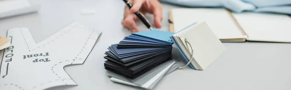 Vista ritagliata del progettista offuscata con penna vicino campioni di colore e modello di cucito, banner — Foto stock