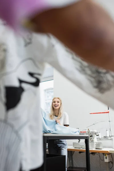 Cheerful fashion designer showing sample of material to blurred colleague — Stock Photo