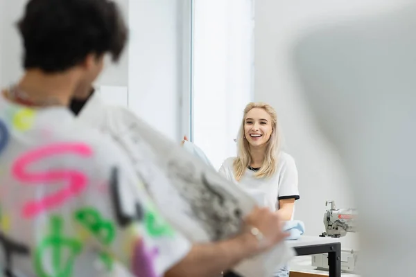 Vista posterior de diseñador de moda borrosa mostrando ropa a colega alegre - foto de stock