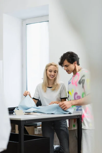 Lächelnde Modeschöpfer beim Betrachten von Gewebeproben auf verschwommenem Vordergrund — Stockfoto