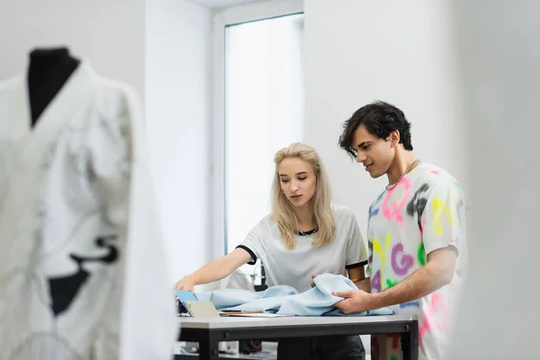 Couple of young designers choosing colors and fabric near mannequin on blurred foreground — Stock Photo