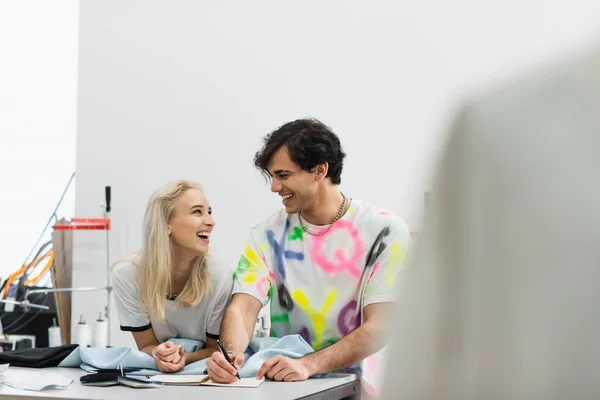 Cheerful designers talking in atelier near samples of cloth and colors, blurred foreground — Stock Photo