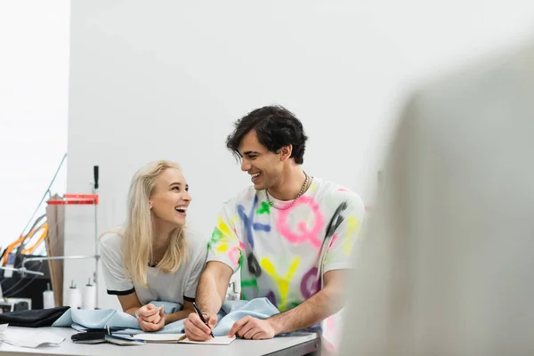 Designers joyeux parler dans l'atelier près des échantillons de tissu et de couleurs, au premier plan flou — Photo de stock