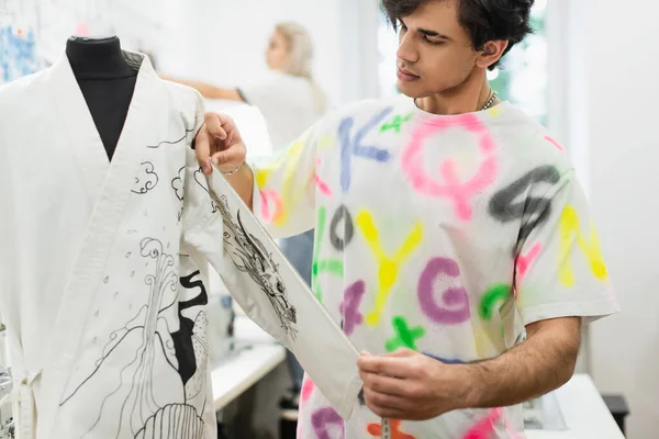Модный дизайнер смотрит на кимоно на манекене рядом с коллегой работает на размытом фоне — стоковое фото