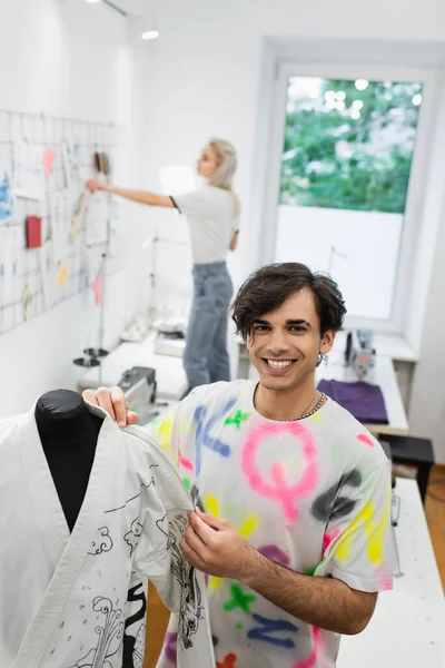 Diseñador feliz medir kimono cerca colega trabajando sobre fondo borroso - foto de stock