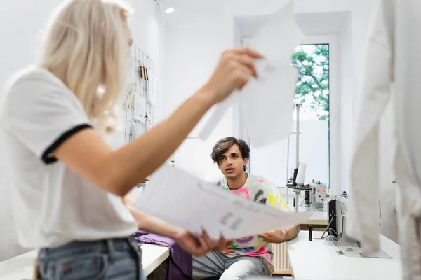 Jovem designer olhando para colega com papéis em primeiro plano desfocado — Fotografia de Stock