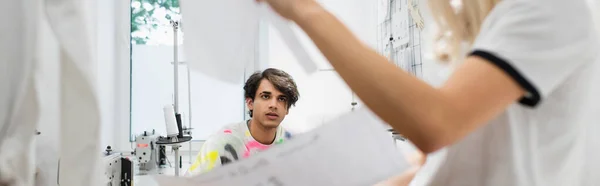 Young fashion designer looking at blurred colleague in tailor shop, banner — Stock Photo