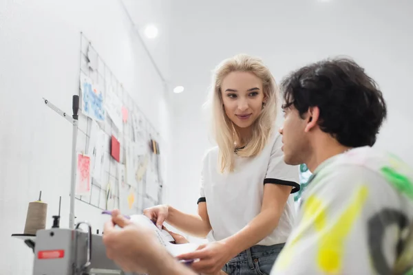 Junge Modedesignerin zeigt Schnittmuster zu verschwommenem Schneider — Stockfoto