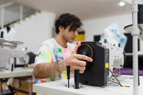 Giovane sarto offuscata regolazione macchina da cucire in officina di moda — Foto stock