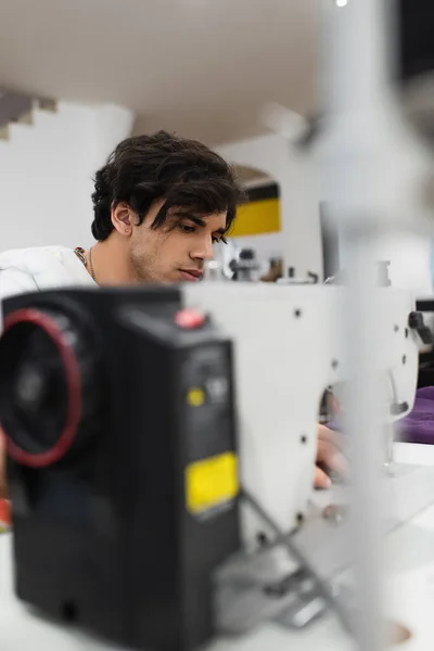 Селективное внимание молодого портного, работающего над швейной машинкой в ателье моды — стоковое фото