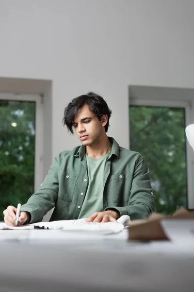 Giovane stilista che disegna su tessuto con pennarello in primo piano sfocato — Foto stock