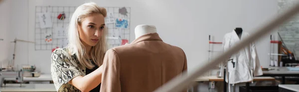 Diseñador de moda rubia trabajando cerca del maniquí en blazer, pancarta - foto de stock