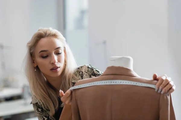 Jovem designer de moda medindo blazer no manequim na oficina de moda — Fotografia de Stock