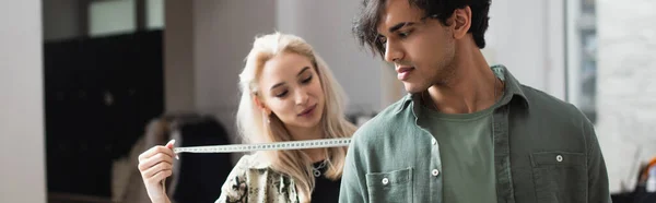 Блондинка модельер измеряет мужчину в ателье, баннер — стоковое фото
