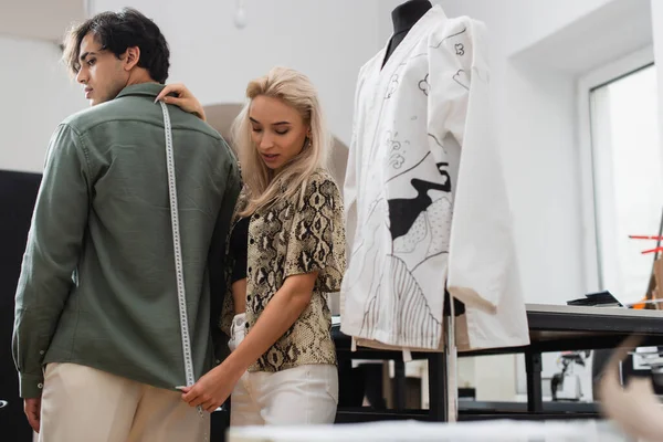 Designer à la mode mesurant jeune homme dans le magasin de tailleur — Photo de stock