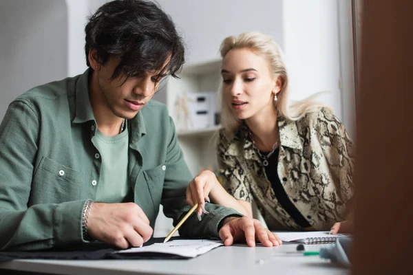 Stilvolle Designerin, die mit Bleistift in der Nähe des Schneiders mit Stoff und Schnittmuster arbeitet — Stockfoto